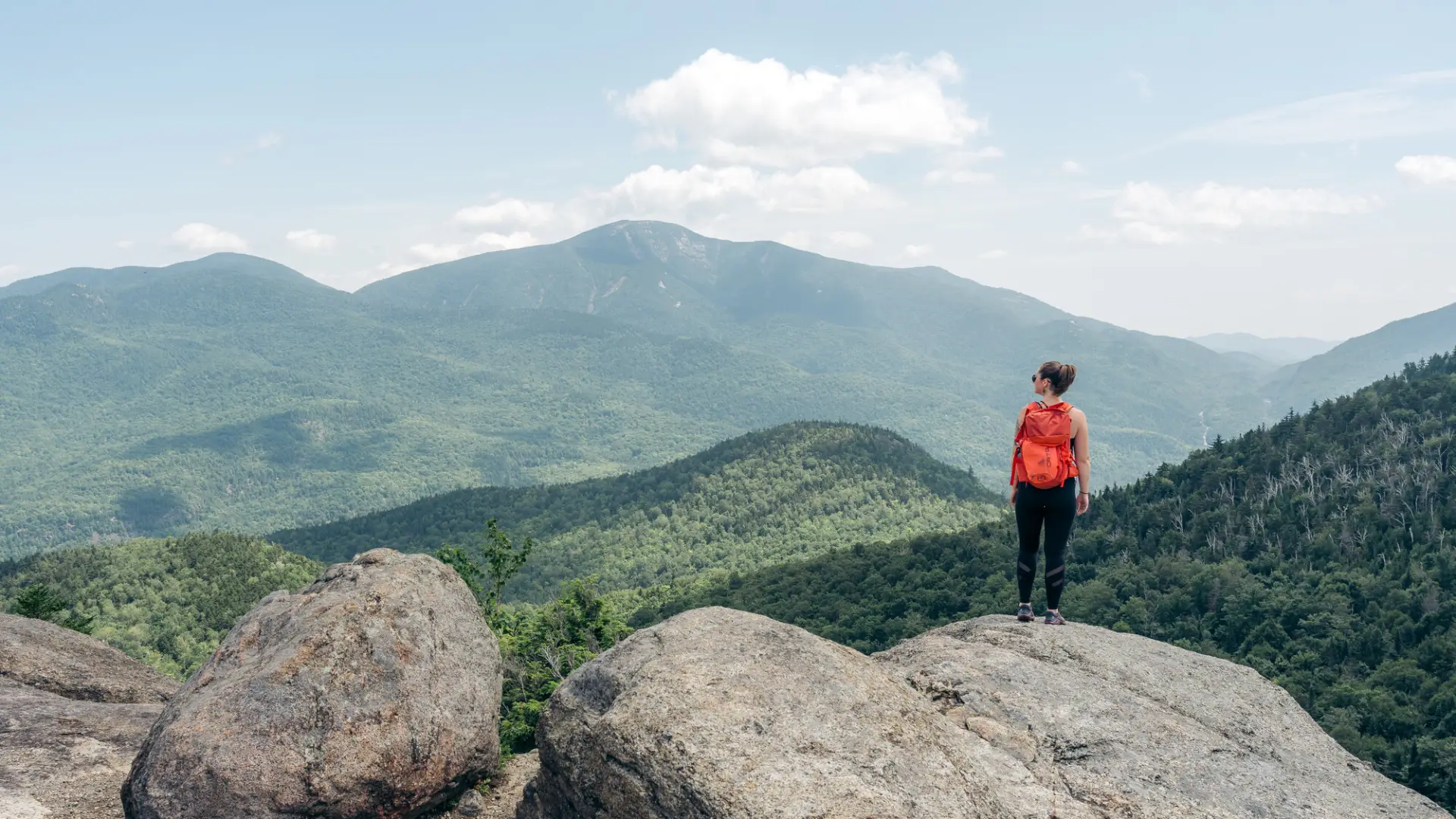 A woman stands on top of a mountain in summer
